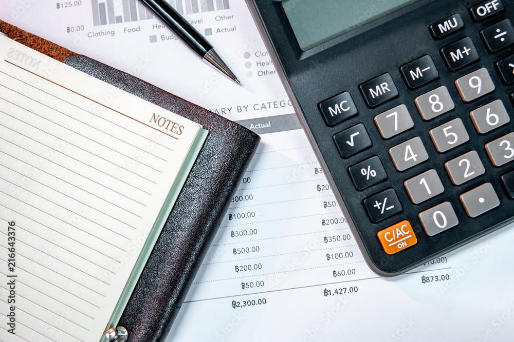 Calculator, pen, blank lined paper page of notebook and summary report paperwork with bar graph and table. Financial data analysis. Business planning and management concept Calculator, pen, blank lined paper page of notebook and summary report paperwork with bar graph and table. Financial data analysis. Business planning and management concept
