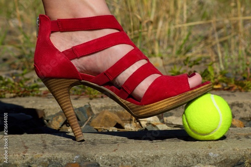 Ladies leg - foot in the court shoe and a tennis ball.A woman in a pump shoe standing on a yellow tennis ball. Woman standing on overgrown train track.