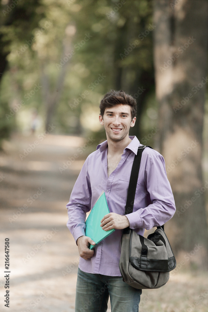 successful guy student with a bag and a clipboard on the background of the Park successful guy student with a bag and a clipboard on the background of the Park