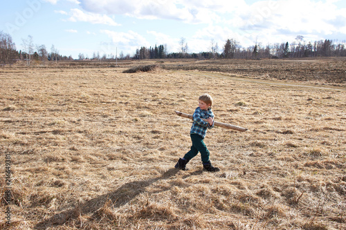 Boy carrying wooden pole across field photo