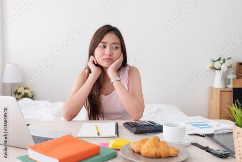 Asian woman freelancer rest chin on hand with bore feeling with work problem with laptop on mess table.work at home concept.stress working.