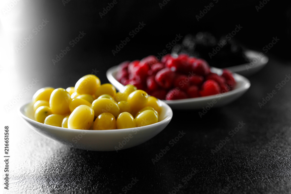 raspberry, blackberries and dogeberry in white plate on black background