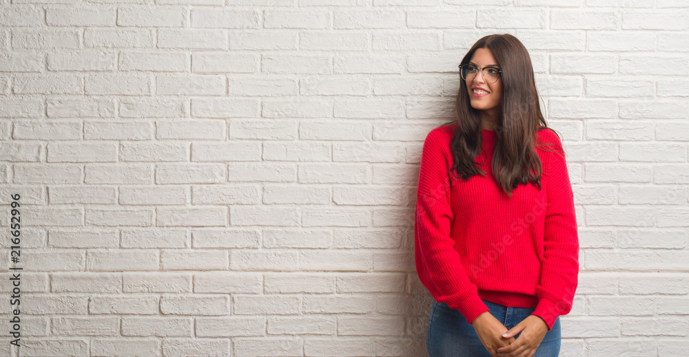 Young brunette woman standing over white brick wall looking away to side with smile on face, natural expression. Laughing confident. Young brunette woman standing over white brick wall looking away to side with smile on face, natural expression. Laughing confident.