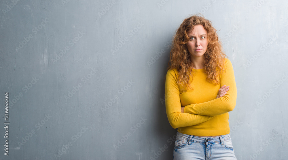 Young redhead woman over grey grunge wall skeptic and nervous, disapproving expression on face with crossed arms. Negative person. Young redhead woman over grey grunge wall skeptic and nervous, disapproving expression on face with crossed arms. Negative person.