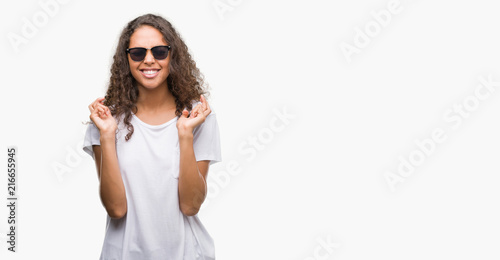 Young hispanic woman wearing sunglasses smiling crossing fingers with hope and eyes closed. Luck and superstitious concept.
