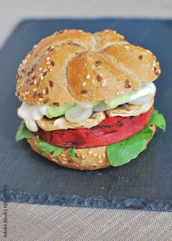 Vegan burger with beetroot, arugula, onion, mushrooms, avocado, black stone background.