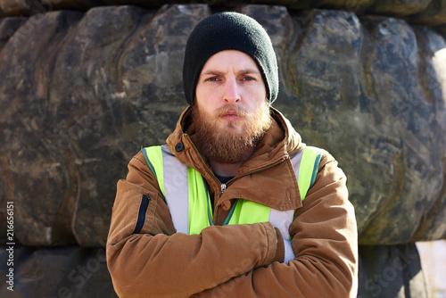 Fototapeta Portrait of tough bearded  frontier worker standing with arms crossed and lookin