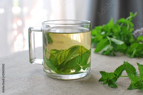 Fresh peppermint leaves tea served in glass cup on linen tablecloth.