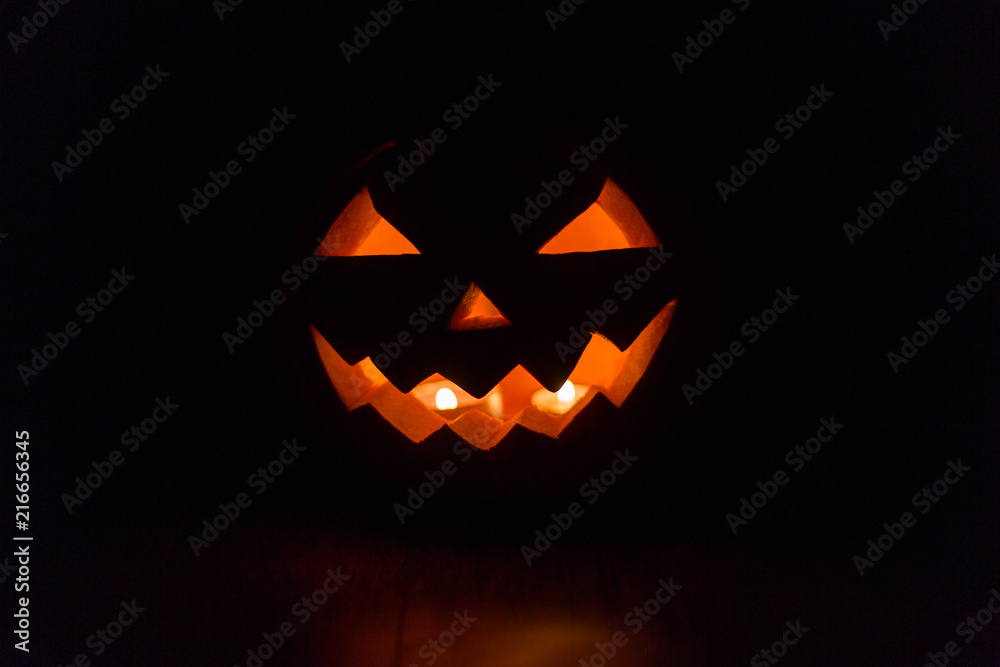 Fototapeta premium halloween and holidays concept - spooky jack-o-lantern or carved pumpkin lantern burning in darkness