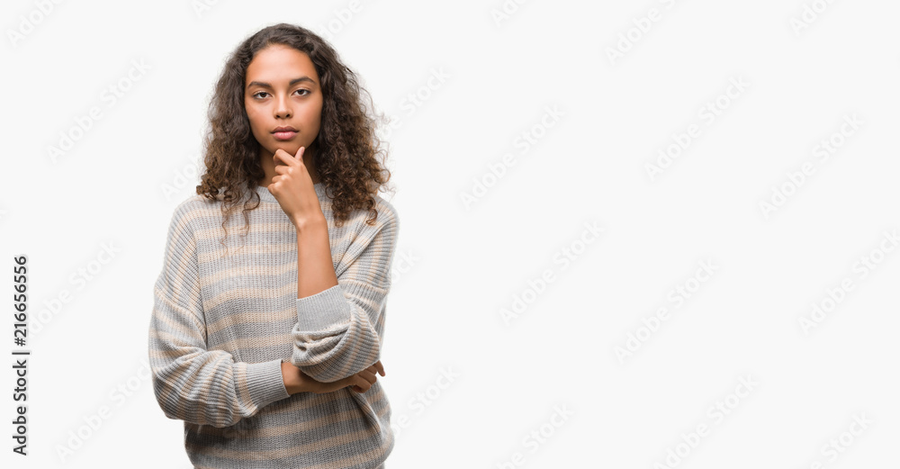 Beautiful young hispanic woman wearing stripes sweater looking confident at the camera with smile with crossed arms and hand raised on chin. Thinking positive. Beautiful young hispanic woman wearing stripes sweater looking confident at the camera with smile with crossed arms and hand raised on chin. Thinking positive.