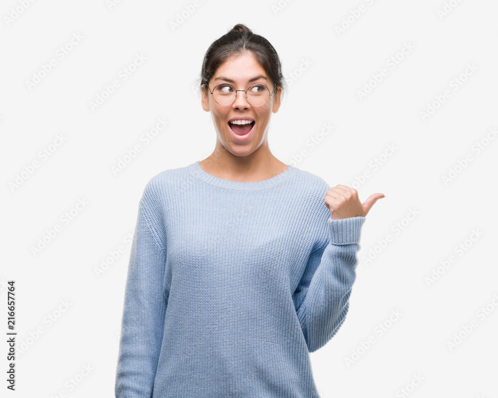 Young beautiful hispanic woman wearing a bun pointing and showing with thumb up to the side with happy face smiling Young beautiful hispanic woman wearing a bun pointing and showing with thumb up to the side with happy face smiling