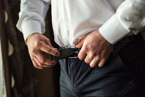 Businessman putting on a belt  fashion and clothing concept groom getting ready in the morning before ceremony