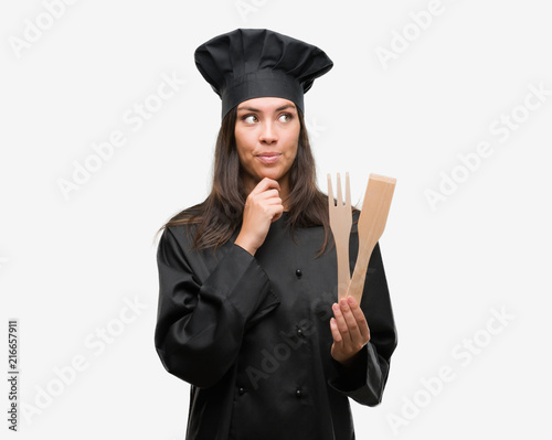 Young hispanic cook woman wearing chef uniform serious face thinking about question, very confused idea