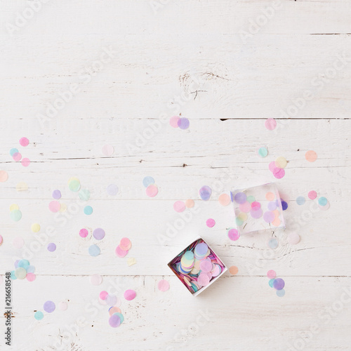 Top view on box full of colorful confetti on white wooden table or background.