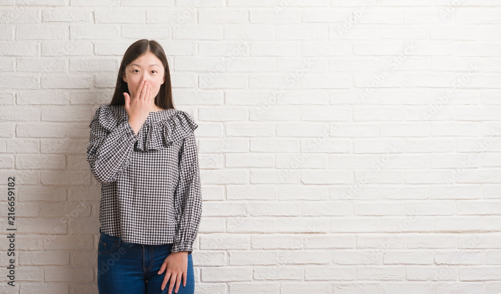 Young Chinese woman over brick wall cover mouth with hand shocked with shame for mistake, expression of fear, scared in silence, secret concept Young Chinese woman over brick wall cover mouth with hand shocked with shame for mistake, expression of fear, scared in silence, secret concept