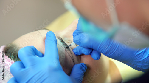 Cosmetologist applying permanent tattooing of eyebrows in beauty salon closeup. Modern microblading workflow and permanent makeup. Beauty, wellness and healthcare concept