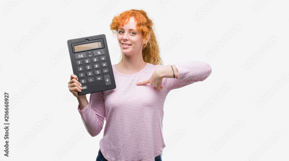 Young redhead woman holding big calculator with surprise face pointing finger to himself Young redhead woman holding big calculator with surprise face pointing finger to himself
