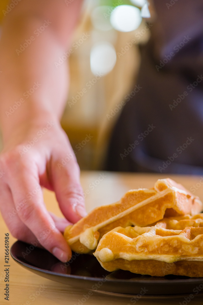 woman hands prepare waffle for serving process.waffle made from dough and batter.tasty dessert sweets waffle served on daylight in cafe background.waffle on black plate.