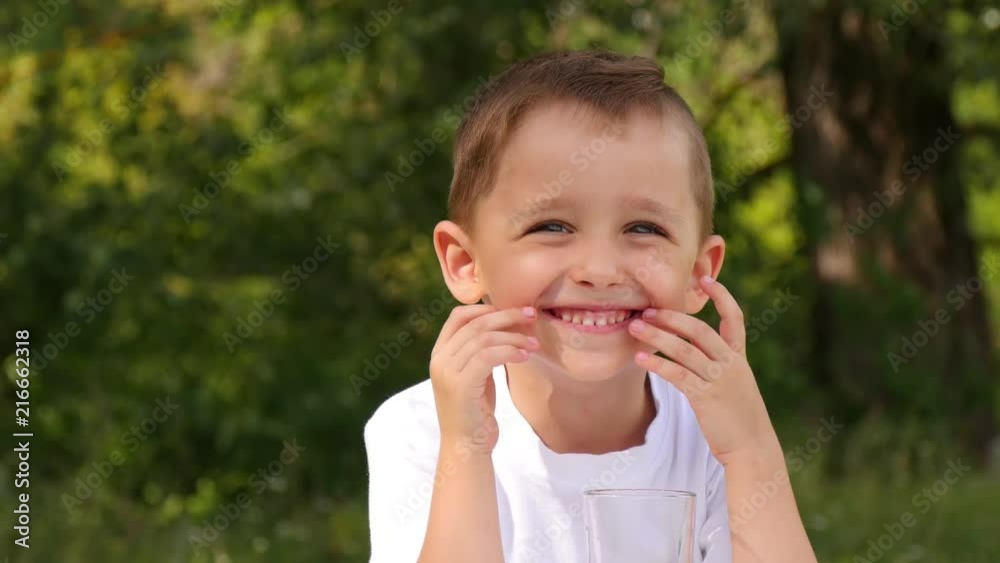 Happy child sitting in the background of nature and drinking berry juice. Cute boy smile and laugh. Happy child sitting in the background of nature and drinking berry juice. Cute boy smile and laugh.