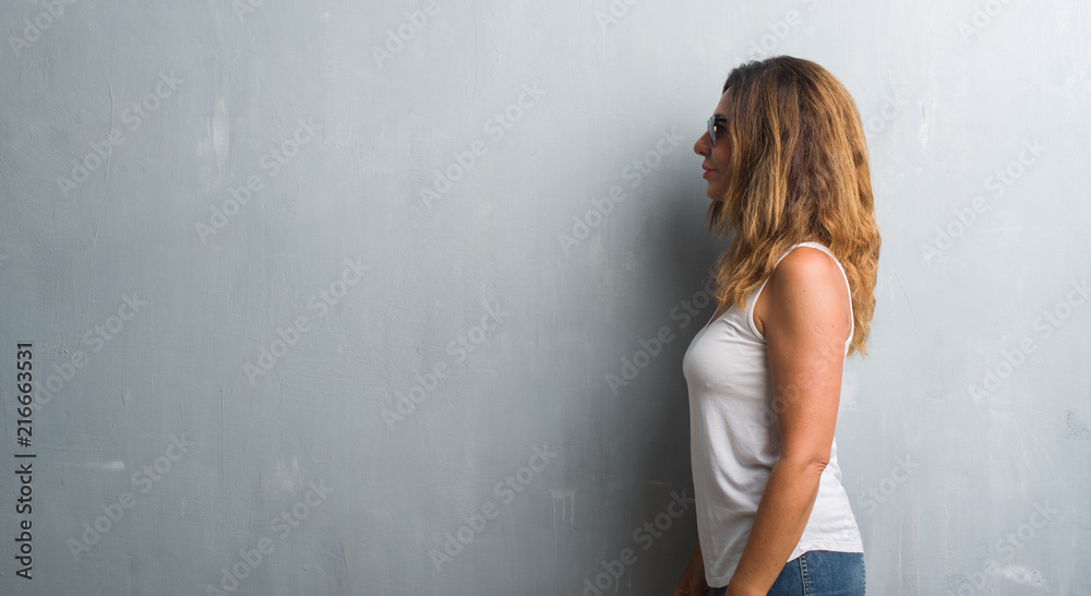 Middle age hispanic woman over grey wall wearing sunglasses looking to side, relax profile pose with natural face with confident smile. Middle age hispanic woman over grey wall wearing sunglasses looking to side, relax profile pose with natural face with confident smile.