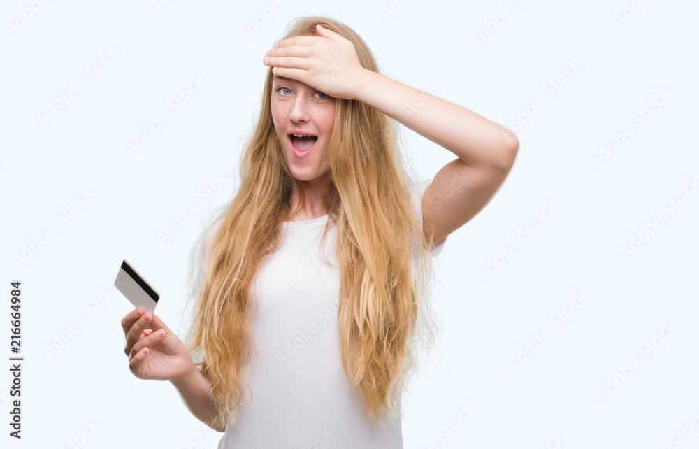 Fototapeta premium Blonde teenager woman holding credit card stressed with hand on head, shocked with shame and surprise face, angry and frustrated. Fear and upset for mistake.