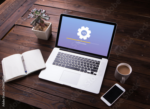 View of Installing update process with gearbox percentage progress and loading bar on laptop / computer with smartphone and office equipment on wooden desk background