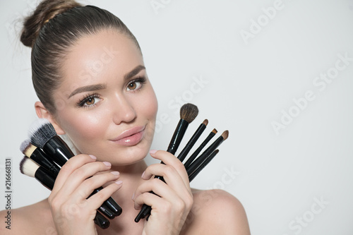 Beauty model girl, makeup artist holding set of make up brushes and smiling. Beautiful brunette young woman with perfect skin and nude make-up. Perfect skin