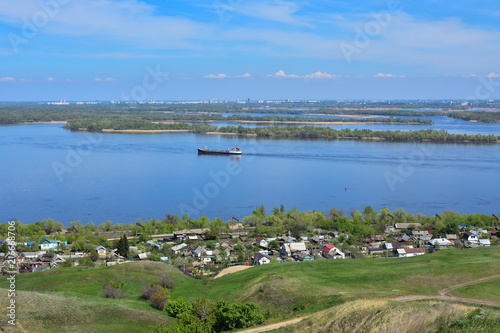 river Volga, coastline, buildings, green vegetation, urban buildings in the background, against the sky and clouds