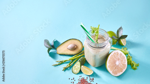 Green smoothie from organic vegetables , fruits, slices of lemon, lime, flax seeds in a glass bowl on blue paper background.