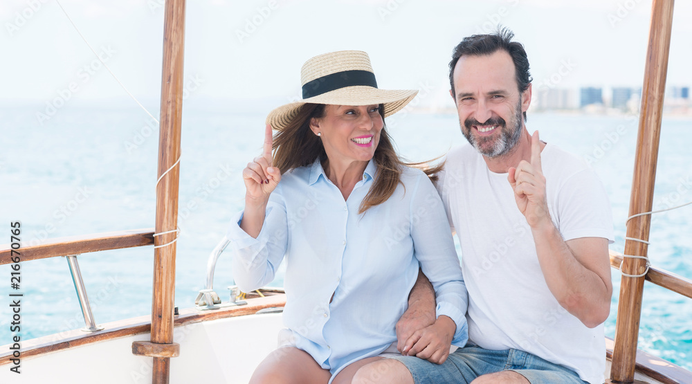 Middle age couple traveling on sailboat surprised with an idea or question pointing finger with happy face, number one