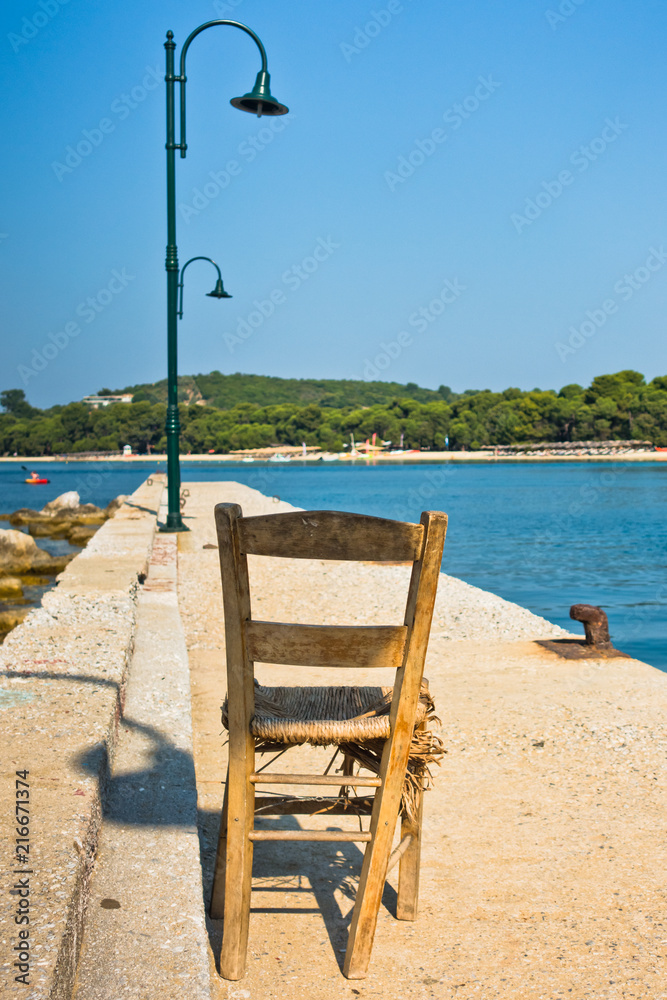 Old wooden chair on a pier in front of Koukounaries beach, morning at Skiathos island, Greece