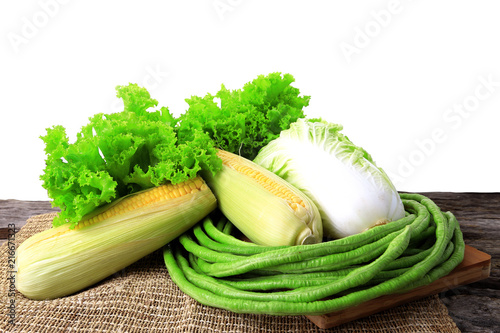 Fresh organic vegetables on wooden table with sack on white color background. Lettuces, Chinese cabbage, Yard long beans, Sweet corn, Foods preparation concept.