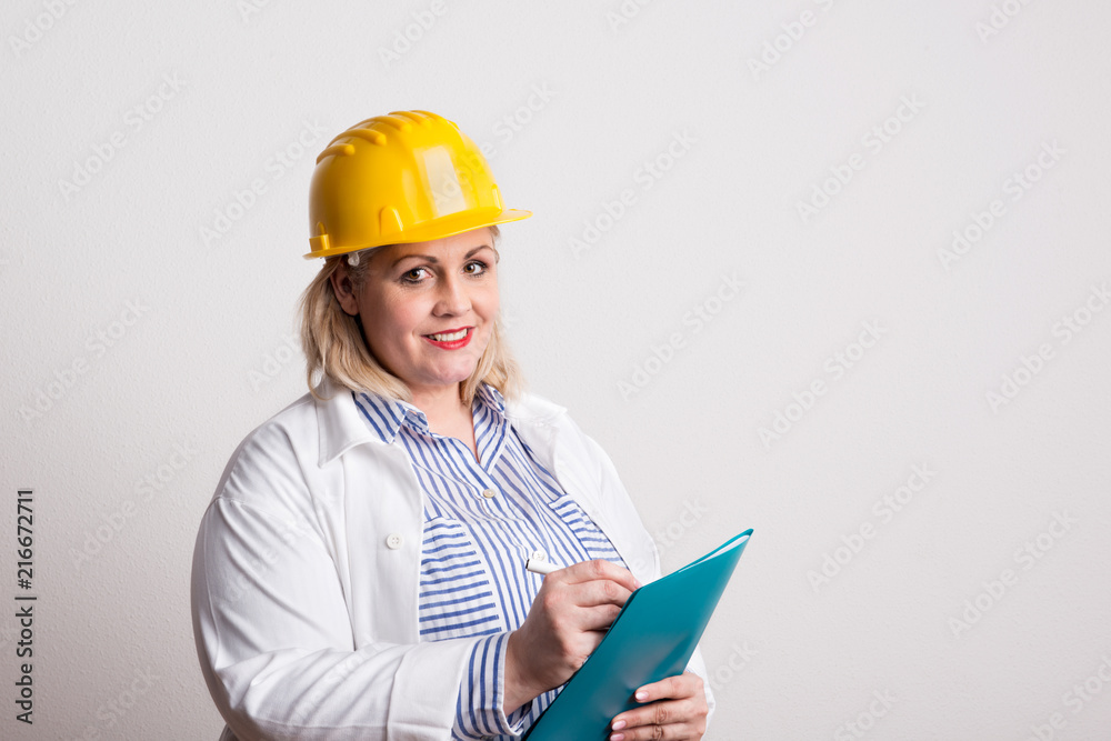 Portrait of an attractive overweight woman with yellow helmet in a studio. Portrait of an attractive overweight woman with yellow helmet in a studio.