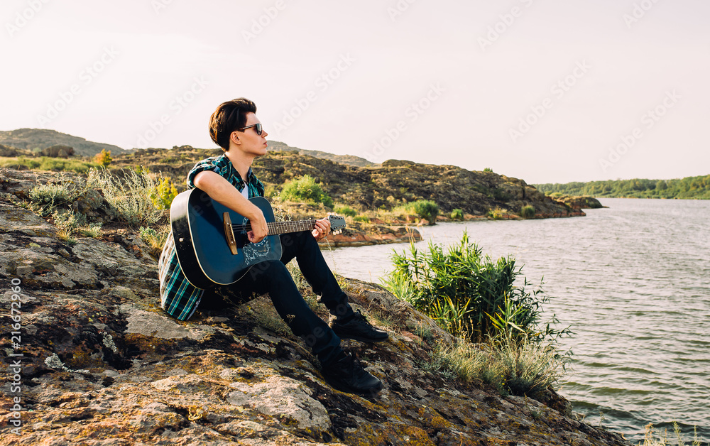 young man plays guitar on nature near lake