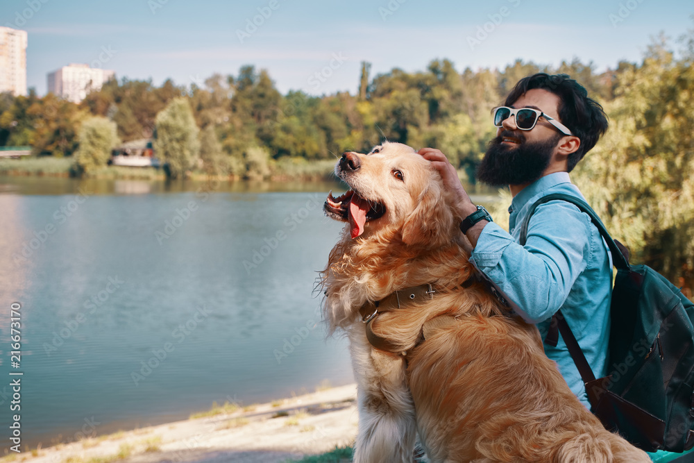 Young man sitting with his dog on the chair in the park, enjoyin Young man sitting with his dog on the chair in the park, enjoyin