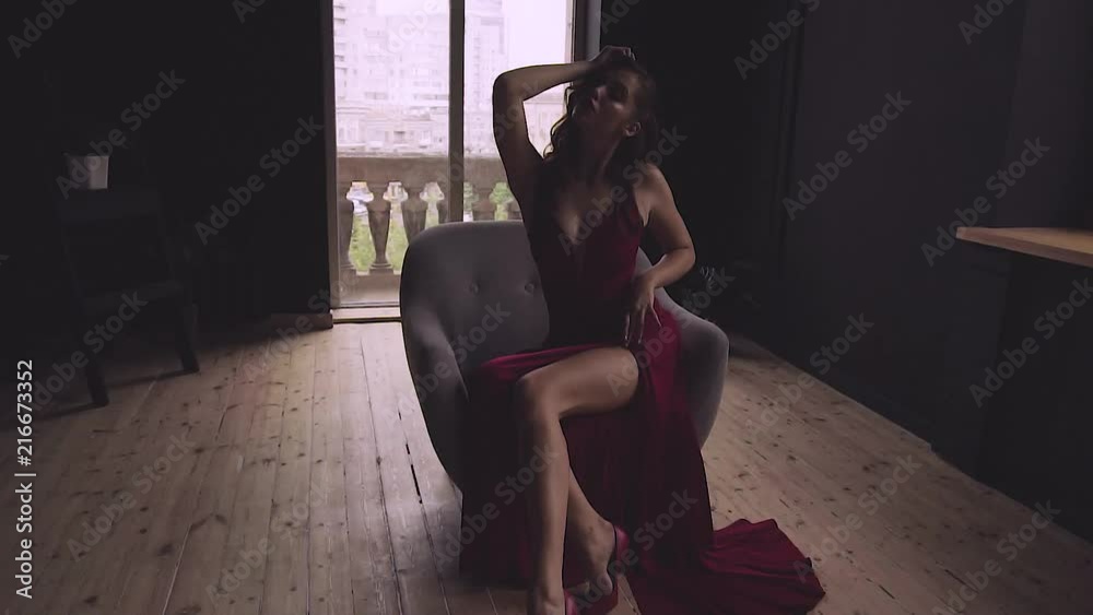 A gorgeous red-haired lady in an elegant red dress is sitting in a chair. A gorgeous red-haired lady in an elegant red dress is sitting in a chair.