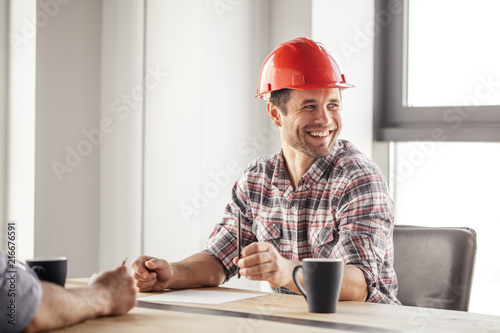 laughing beaded constructor holding a pen and looking aside during the coffee break photo