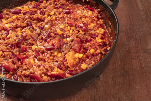 A large cast iron pan with chili con carne, on a dark background with copy space
