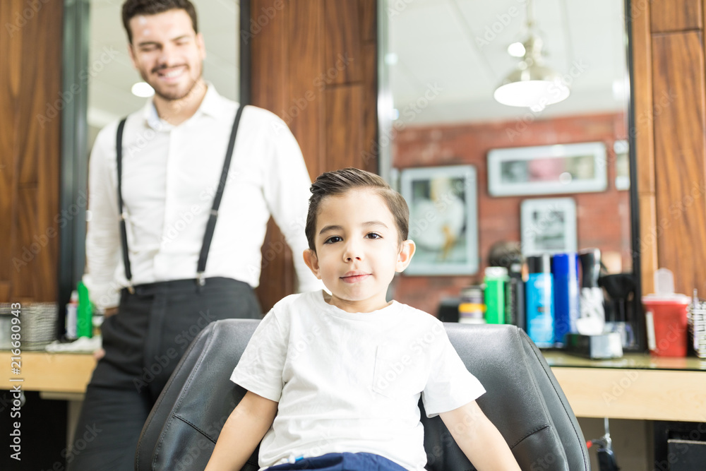Obraz premium Stylish Boy Sitting On Chair While Barber Standing In Shop