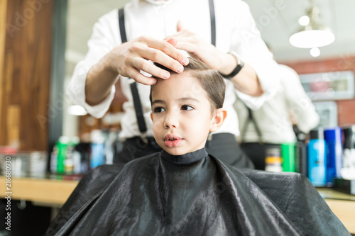 Boy Looking Away While Hairdresser Styling His Hair In Shop