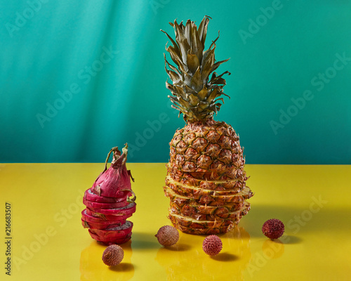 Tropical Pineapple fruit single whole and dragon fruit, pitaya made up of sliceson and litchi fruits on a duotone yellow-blue background photo