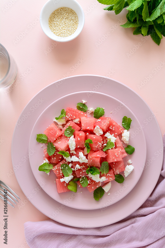Summer watermelon salad with feta cheese, sesame seeds and mint leaves on pink plate. Healthy eating concept