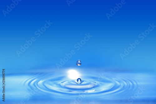 Closeup on double drop of water falling in a blue liquid and create circular wave.