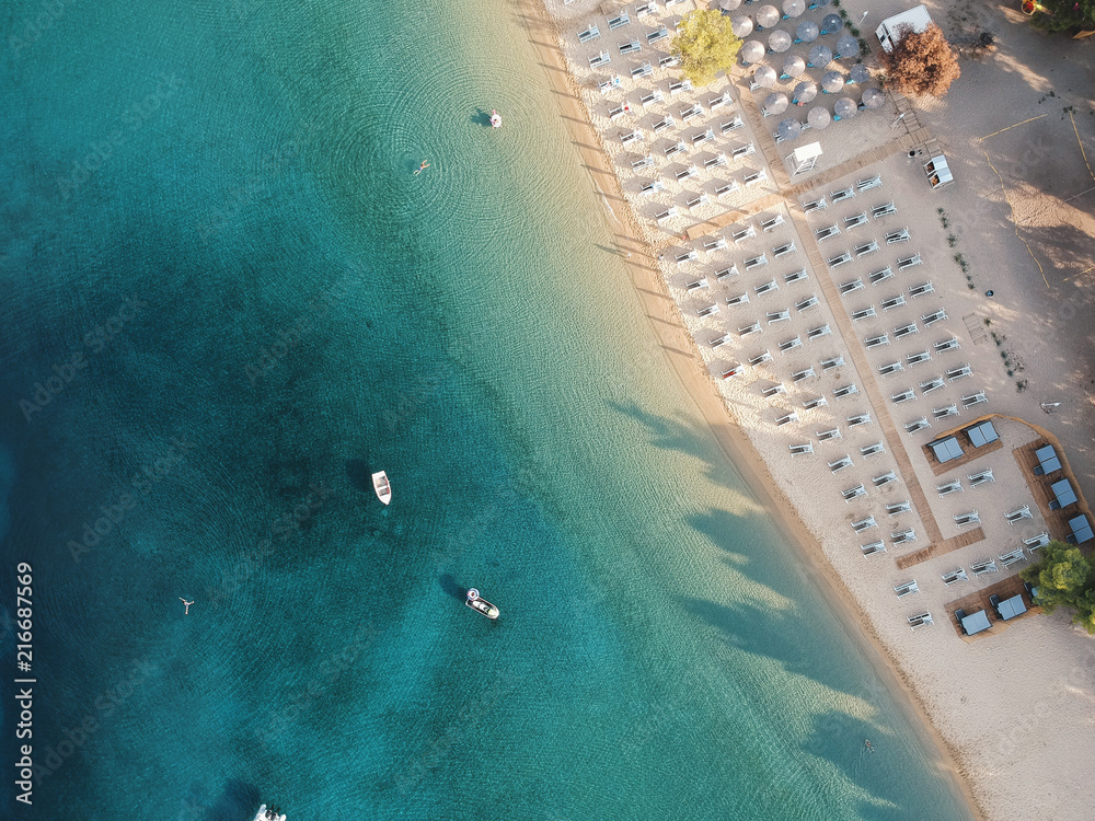 Aerial view of bright turqoise water and beach with a few people.