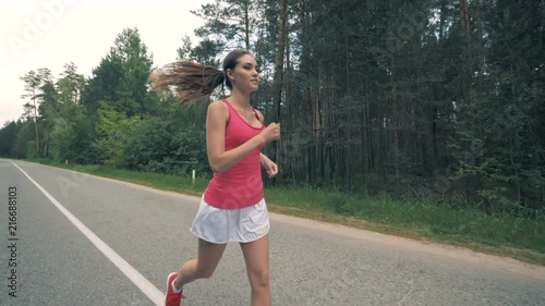 Forest road with a young lady running along it. Healthy slim young sportswoman running. photo