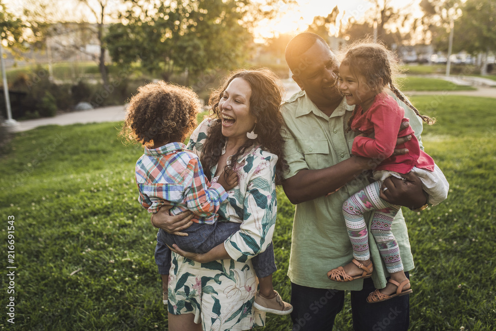 © Cavan Images - Cheerful parents carrying children on field at park during sunset