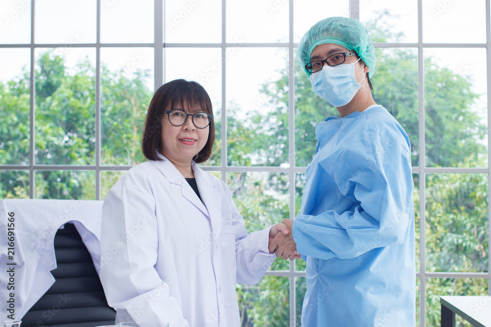 Obraz premium Two happy smiling medical people wear white and blue form handshaking at office. Doctors. Teamwork