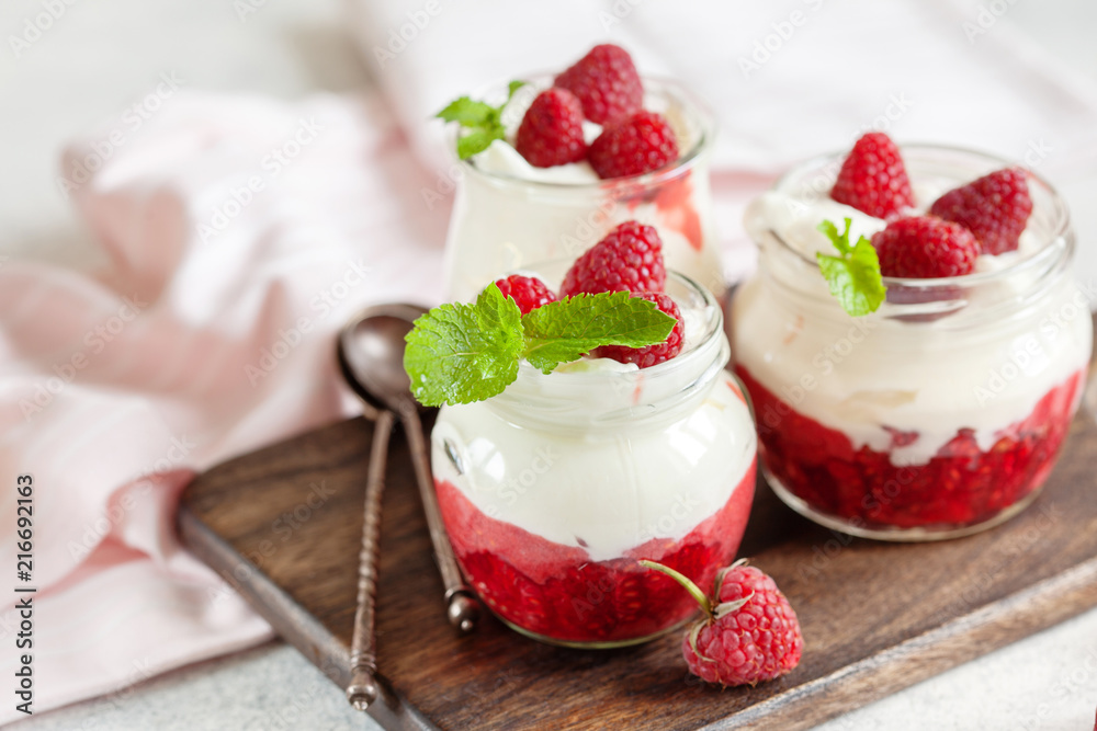 Jars of natural white yogurt with berry sauce decorated with fresh raspberry and mint