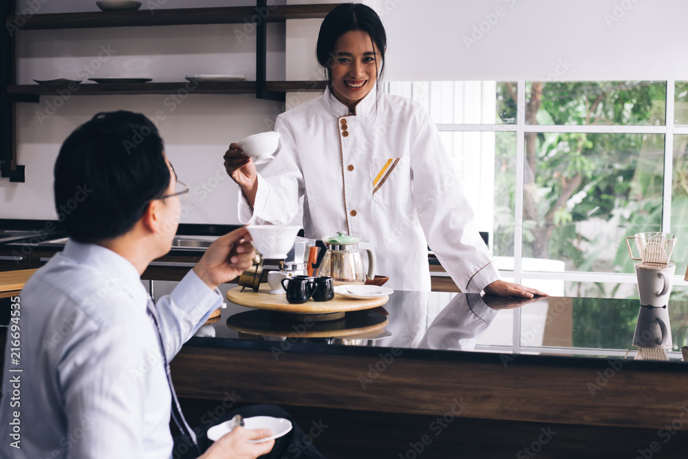 Young female barista making a coffee and talking with smart businessman male customer at cafe restaurant