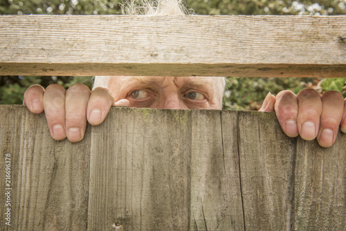 Fotografie Mature man spying through a wooden fence in the garden